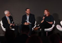TTS Director Ann Lewis holds a microphone and sits in a white chair on stage at Scoop News group's CyberTalks in Washington. She is joined by GDIT's vice president of cyber, Matthew Mcfadden, and Scoop News Group's senior vice president of content strategy, Wyatt Kash, who are also seated.