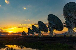 Photo shows a row of large radio antennas that make up the National Science Foundation's Very Large Array. The antennas appear in silhouette at dusk.