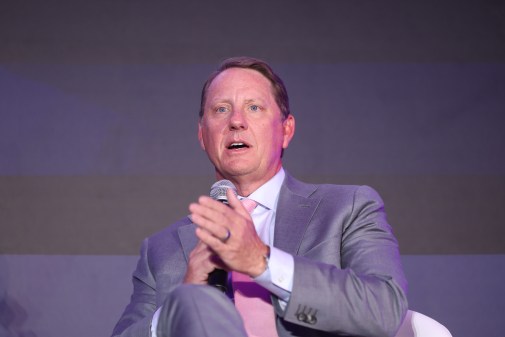 Man in suit speaks on stage with a microphone