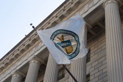 The circular Department of Commerce seal appears on a white flag attached to the front of the agency's federal-style building. The flag blows in the wind, displaying a majority of the seal.