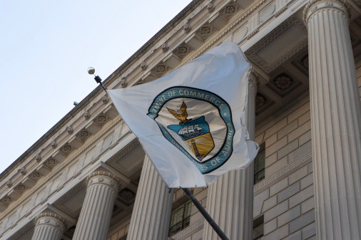 The circular Department of Commerce seal appears on a white flag attached to the front of the agency's federal-style building. The flag blows in the wind, displaying a majority of the seal.