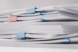 A stack of documents and papers on white desk with laptop