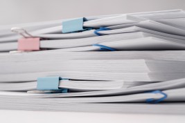A stack of documents and papers on white desk with laptop