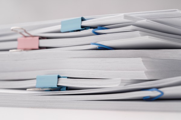 A stack of documents and papers on white desk with laptop