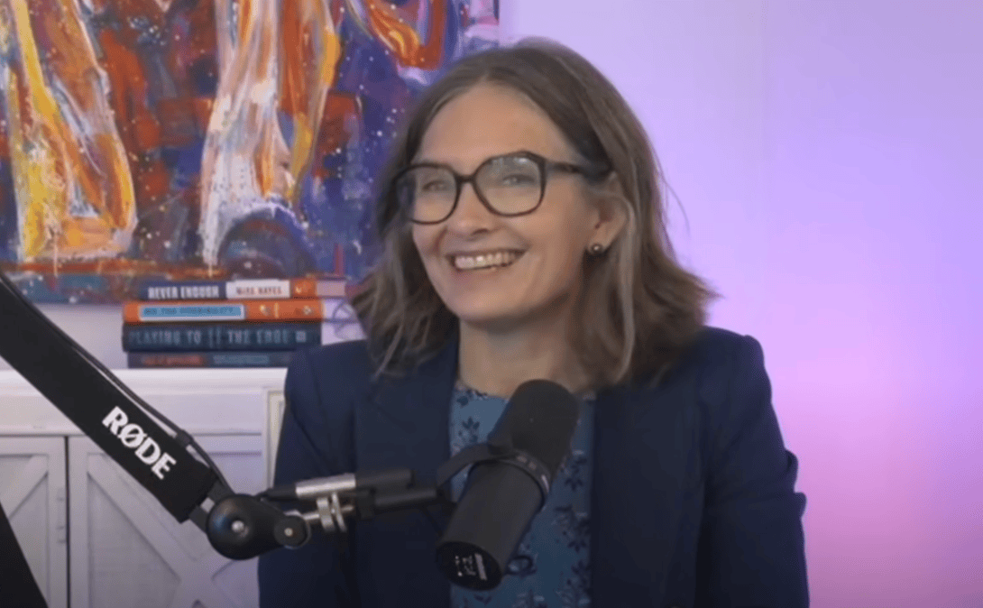 Denice Ross is pictured on an episode of the DailyScoop Podcast. She is sitting in front of a microphone and is smiling.