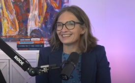 Denice Ross is pictured on an episode of the DailyScoop Podcast. She is sitting in front of a microphone and is smiling.